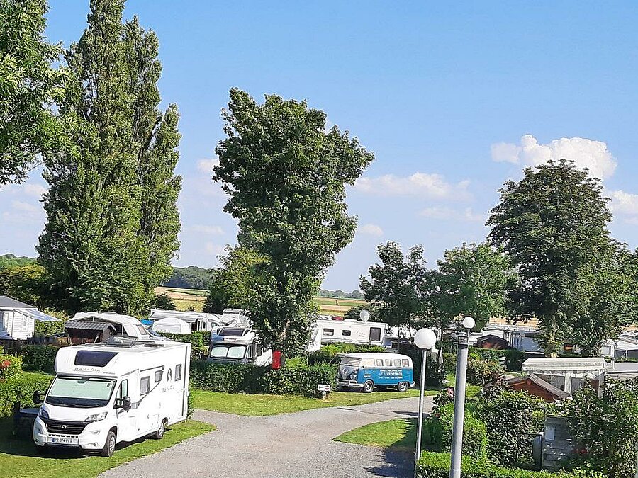 Ruime staanplaatsen voor campers en busjes, omringd door groen op een camping in de Picardië, met rust en comfort voor een vakantie dicht bij de natuur.