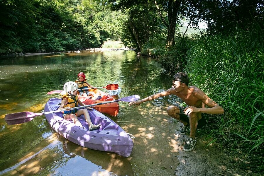 Kinderen kajakken op een rivier bij een camping aan het meer, samen genieten van natuur en watersport.