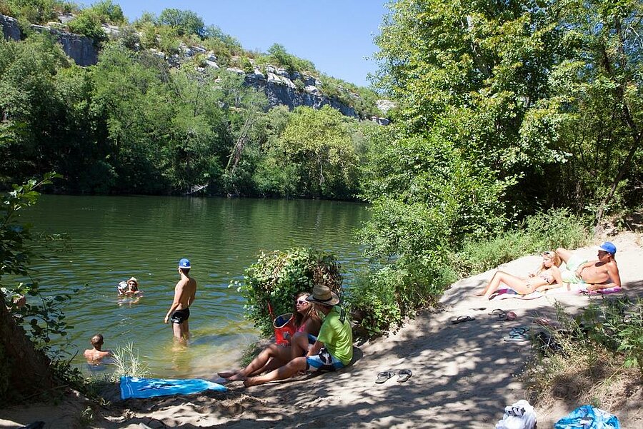 Families die genieten van een zwempartij en ontspannen op een schaduwrijke oeverstrand langs de rivier, vlakbij de Ardèche-kloof.