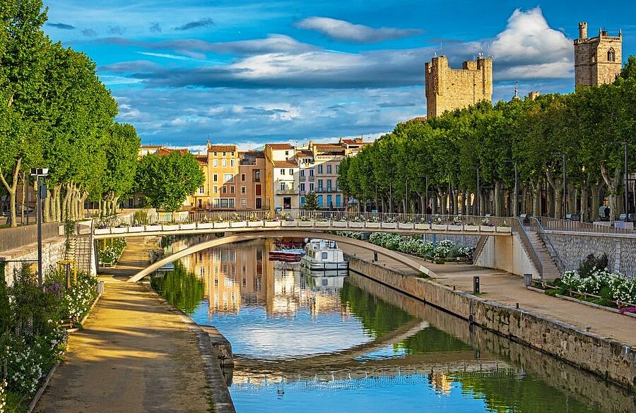 Uitzicht op het Canal de la Robine in Narbonne, omzoomd door bomen en gedomineerd door de middeleeuwse toren, vlakbij een natuurcamping.