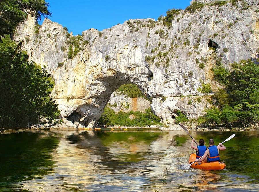 Kanoën onder de Pont d’Arc, een iconische natuurlijke boog in de Ardèche-kloof, een regio om te verkennen tijdens een vakantie op een campsite.