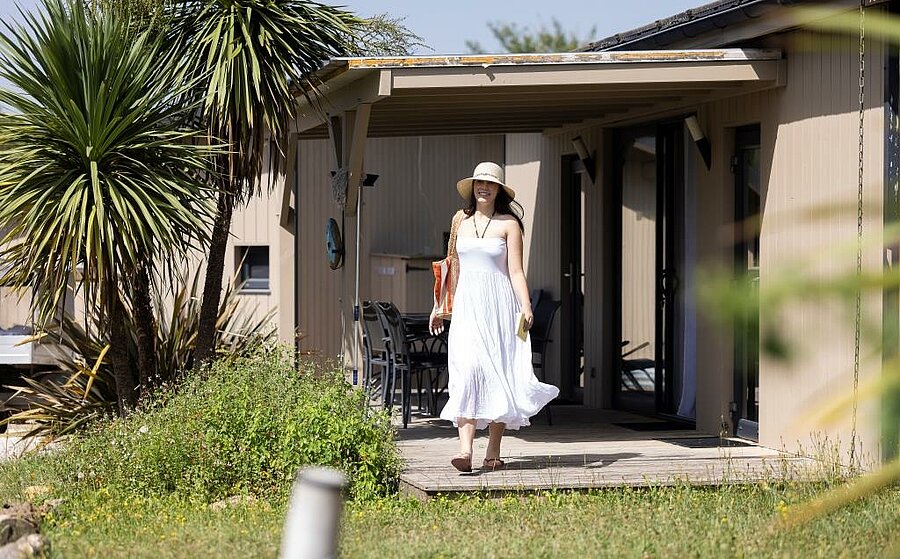 Vrouw in witte jurk verlaat modern chalet met overdekt terras op een natuurcamping bij Toulouse.