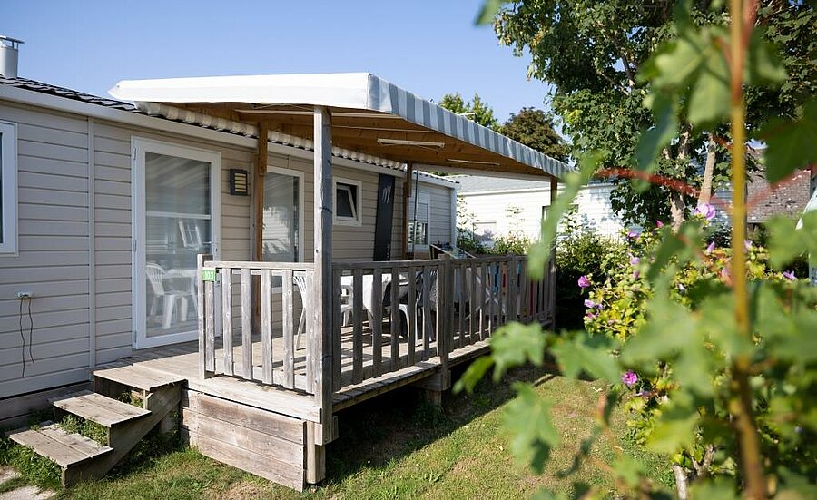 Stacaravan met houten terras op een camping bij Cayeux-sur-Mer, comfortabele accommodatie in een groene omgeving voor gezinsvakanties.