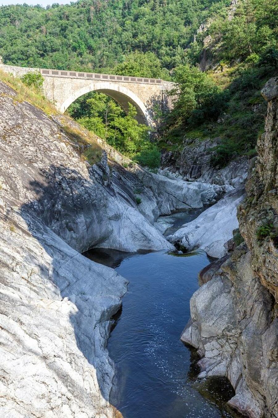 Een pittoreske brug over de Gorges de l’Ardèche, omringd door rotsformaties en weelderige natuur – ideaal voor een kampeervakantie in de Ardèche.
