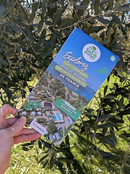 Hand die de Michelin routekaart 2026 van Sites et Paysages campsites vasthoudt, gratis aangeboden om een natuurroadtrip in Frankrijk voor te bereiden.