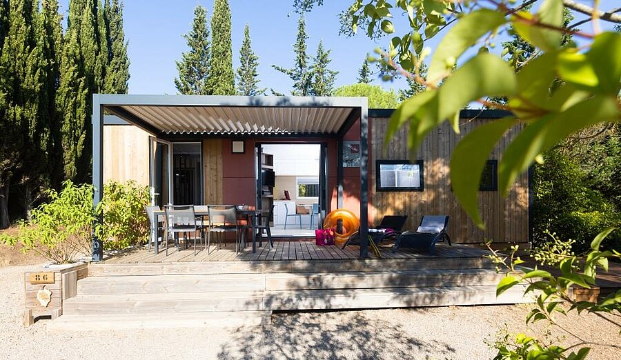 Moderne stacaravan met overdekt terras, tafel en ligstoelen in een groene omgeving bij Carcassonne.