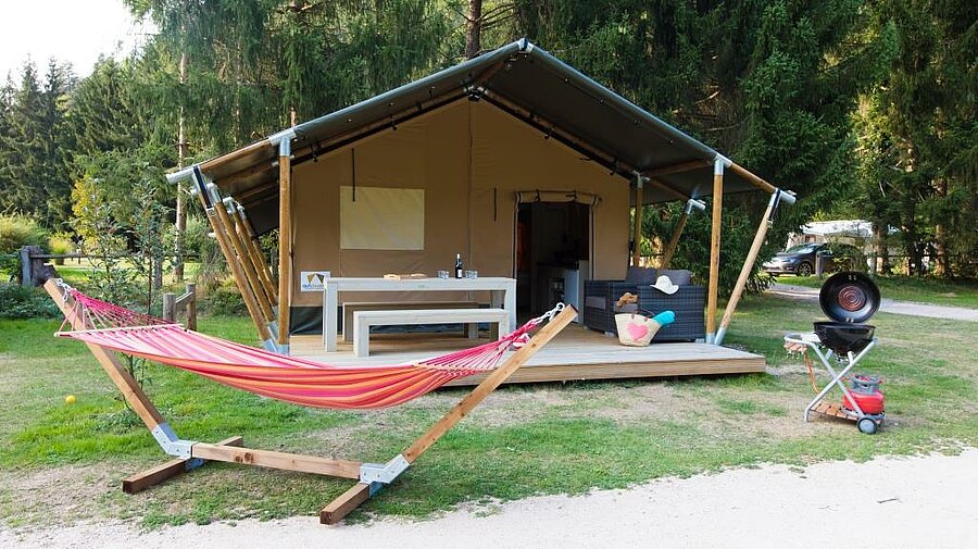 Ingerichte tent met terras en hangmat in een bloemrijke omgeving, ideaal voor een rustige natuurvakantie.