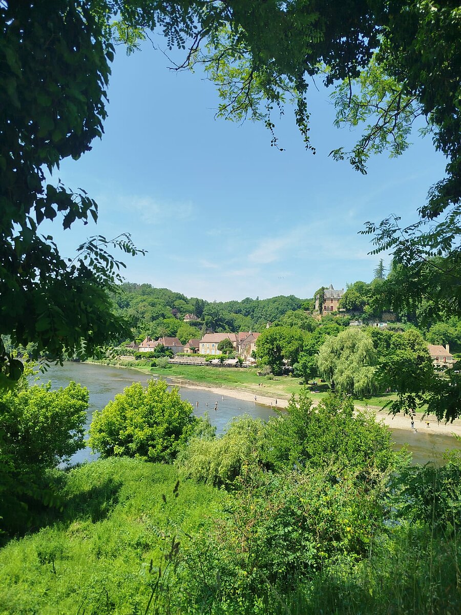Uitzicht op een pittoresk dorp in de Dordogne met de rivier en een natuurlijk strand, dicht bij de campings om de streek te verkennen.