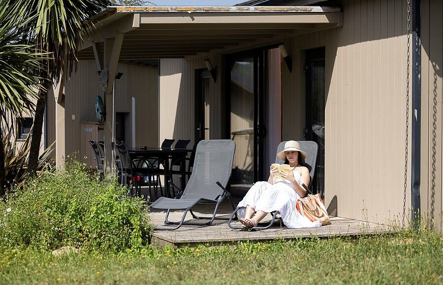 Vakantieganger ontspant op het terras van een comfortabele accommodatie op een rustige 4-sterrencamping.