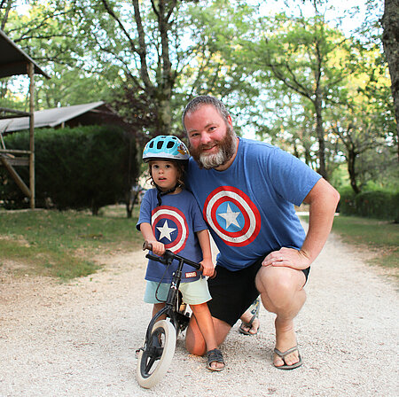 Een vader en zoon met bijpassende T-shirts poseren voor hun milieuvriendelijke accommodatie, als symbool voor concrete hulpmiddelen om actie te ondernemen en bewustwording te creëren rond duurzaam toerisme.