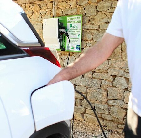 Het opladen van een elektrische auto bij een laadpaal op een charme camping, met een stenen muur op de achtergrond.
