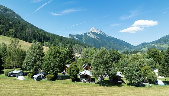 [Translate to Néerlandais:] Vue d’un camping à taille humaine niché au cœur des montagnes, entouré de nature préservée et d’hébergements confortables, idéal pour des vacances en famille.