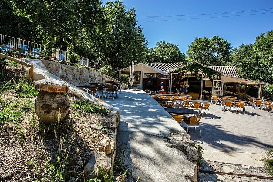Schaduwrijk terras van het restaurant op een camping nabij Vallon Pont d’Arc, ideaal voor een gezellige vakantie in de natuur.