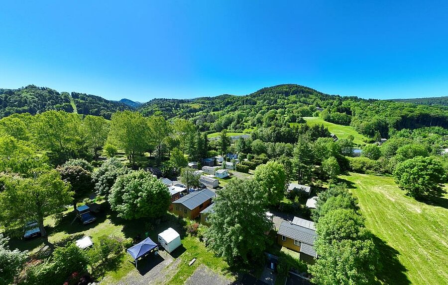 Luchtfoto van een groene camping in het Massif Central met staanplaatsen, chalets en veel natuur.