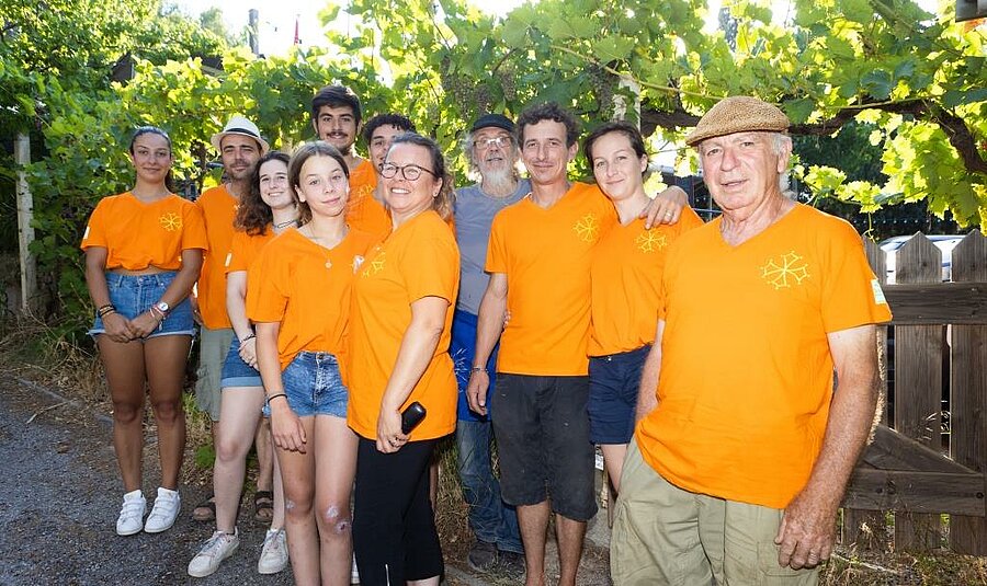 Glimlachend team van een Sites et Paysages charme camping in de Aude, in oranje tenue, klaar om vakantiegangers te ontvangen in een gezellige en familiale sfeer.