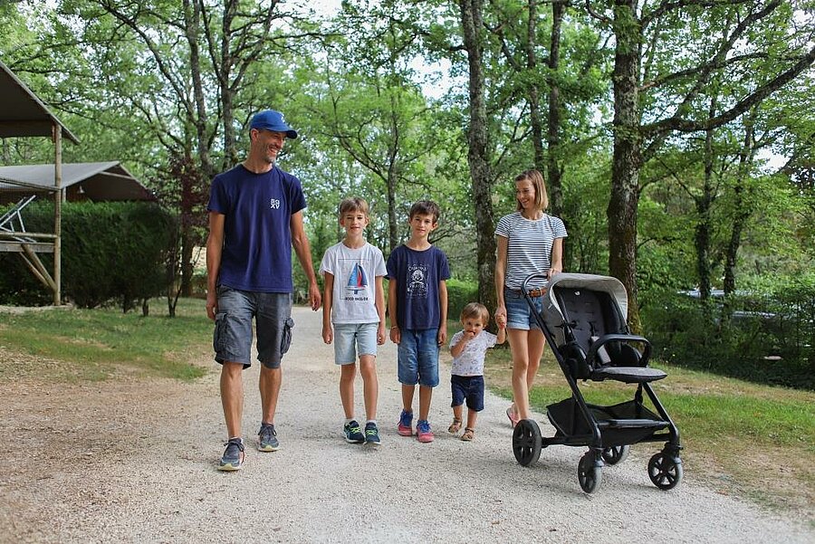 Gezin met kinderen en kinderwagen wandelt op een 3-sterrencamping in Frankrijk, in een veilige en natuurlijke omgeving.