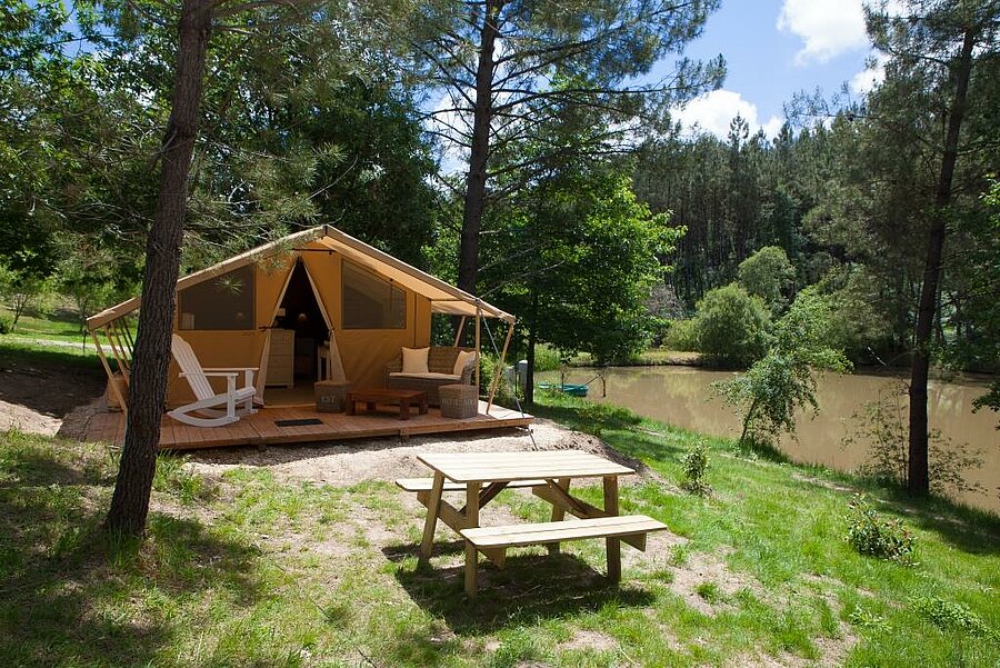 Lodgetent met ingerichte terras, midden in de natuur aan de oever van een vijver, op een camping in de Périgord, in de Dordogne.