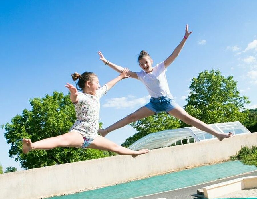 Twee kinderen die spelen op een trampoline in de zon tijdens een kampeerweekend met Pasen bij Sites et Paysages—een moment vol vreugde en vrijheid.