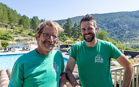 Twee glimlachende eigenaren voor het zwembad, in het hart van een natuurcamping van het Sites et Paysages-netwerk