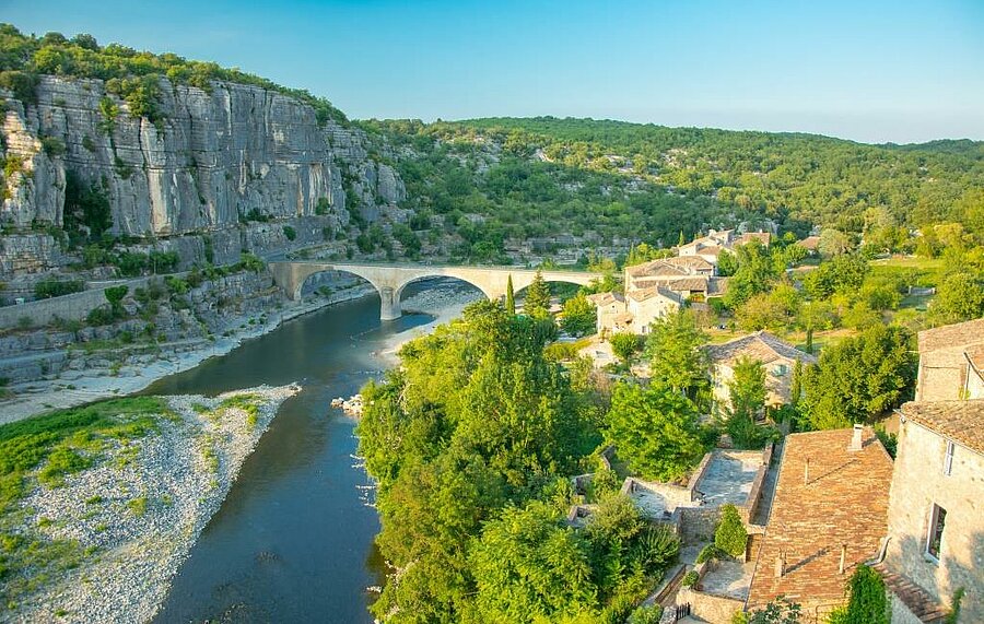 Panoramisch uitzicht op de Gorges de l'Ardèche met een stenen brug en een typisch dorp, Balazuc, omringd door natuur—ideaal voor een kampeervakantie in Auvergne-Rhône-Alpes.