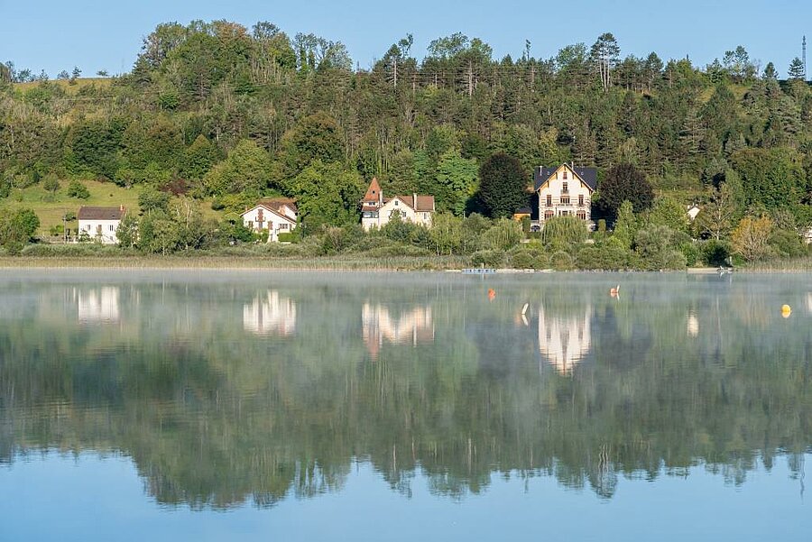 Huizen aan het meer van Clairvaux-les-Lacs met weerspiegeling op het water, ontdek natuur en erfgoed van de Jura.