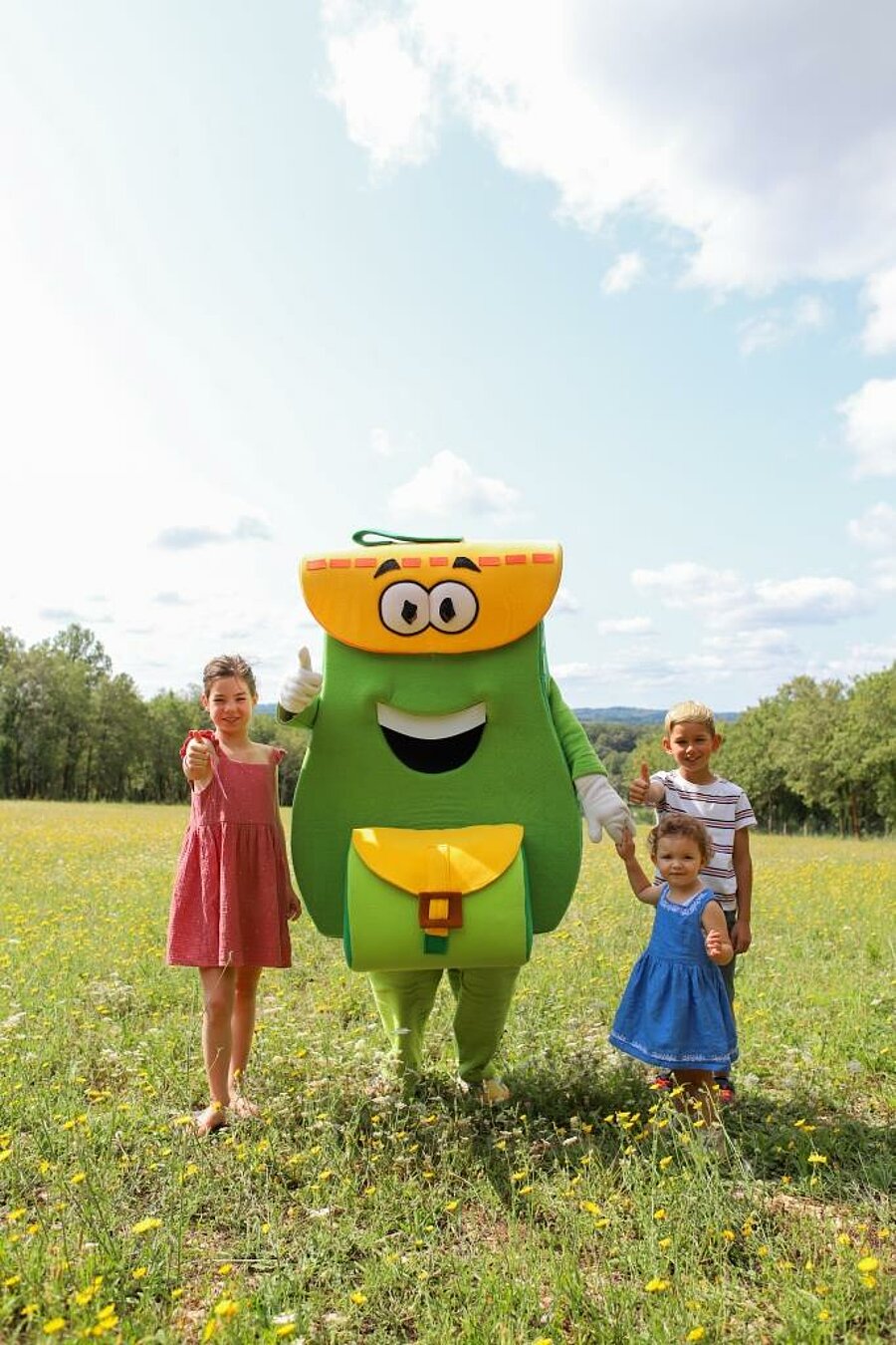 PAKOmascotte met kinderen in een bloemenweide, last minute camping in augustus in zonnige natuur.