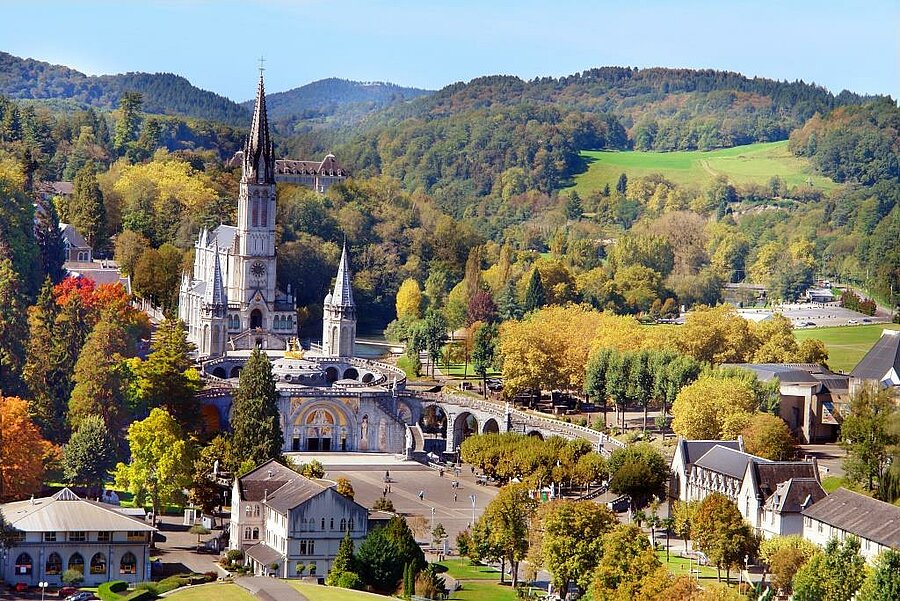 Luchtzicht op het heiligdom en de basiliek van Lourdes, omgeven door bossen en bergen nabij een camping in de Pyreneeën.