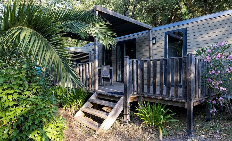 Moderne stacaravan met houten terras en weelderige beplanting, ideaal voor het huren van een stacaravan op een camping in Frankrijk.