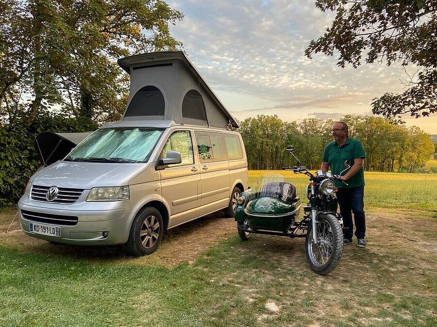Man met zijn zijspan naast een busje op een ruime campingplaats.