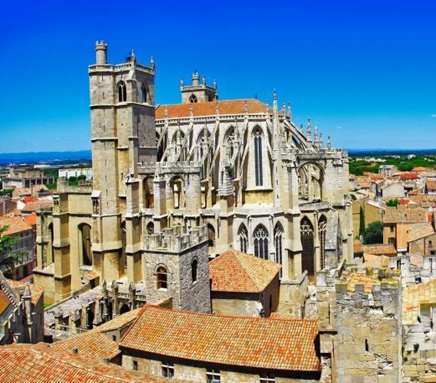 Panorama op de kathedraal van Narbonne en de okerkleurige daken van de stad onder een stralend blauwe lucht, zo typisch voor de Languedoc-Roussillon.