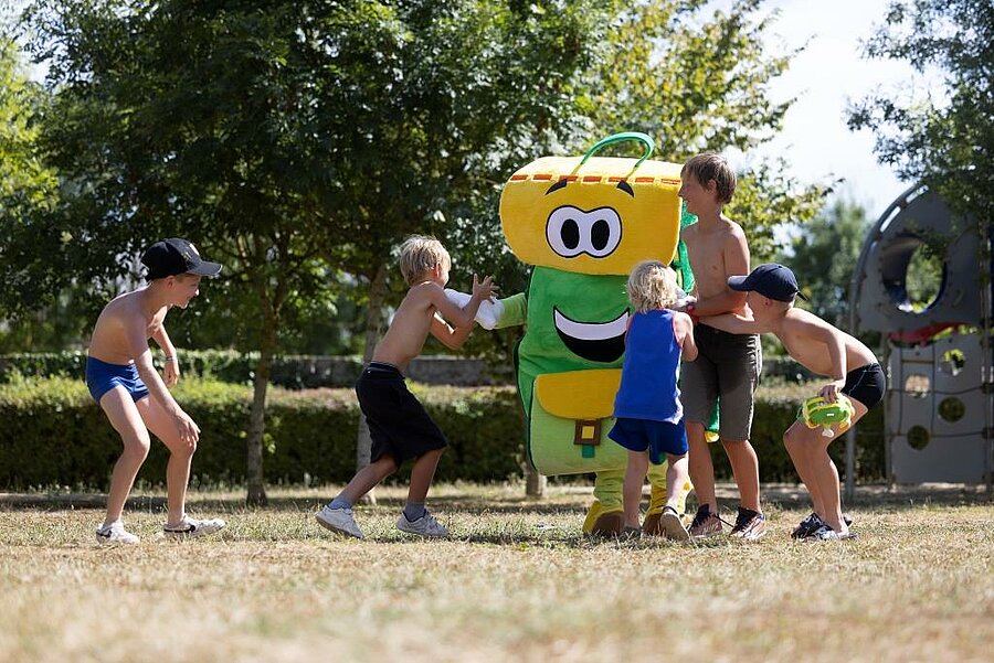 Kinderen spelen met de groene mascotte tijdens een buitenactiviteit op camping L’Étang, vlak bij Angers.