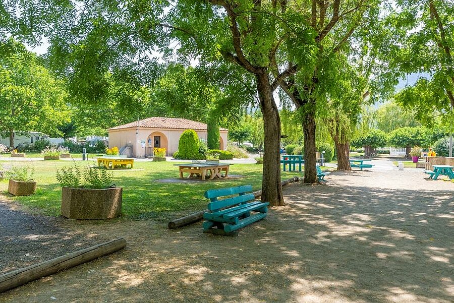 Schaduwrijke zone met banken en picknicktafels op een camping in de Alpes-de-Haute-Provence, ideaal voor een gezinsvakantie midden in de natuur