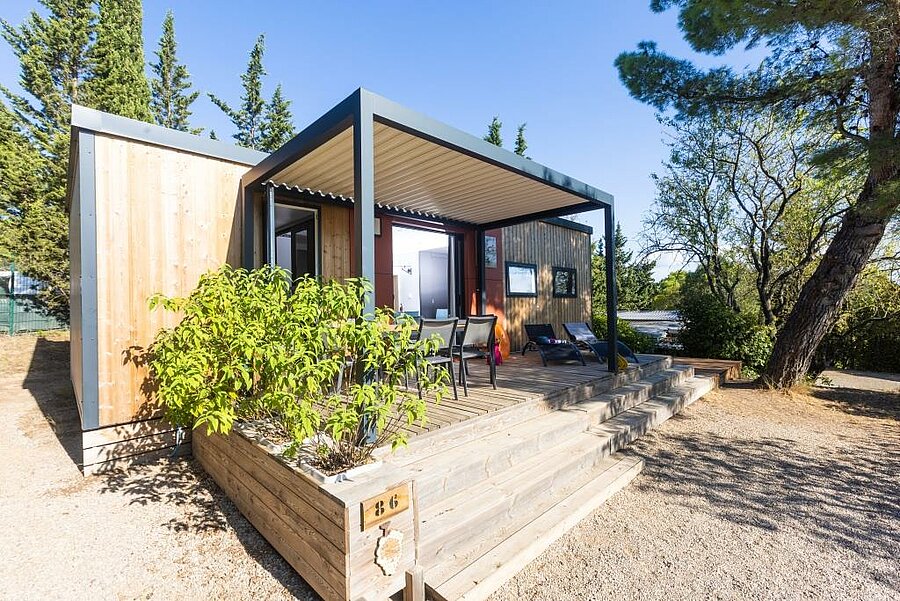 Moderne stacaravan met houten terras en pergola, omringd door groen, op een charme camping in de Languedoc-Roussillon. Een ideale accommodatie voor een vakantie dicht bij de natuur.