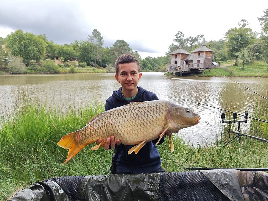 Jonge visser met een grote karper aan een vijver op een camping vissen, hutten op het water op de achtergrond.