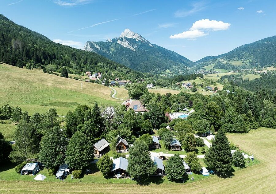 Luchtfoto van een bosrijke campsite in het hart van het Chartreuse-massief nabij Grenoble, met tenten, chalets en bergen op de achtergrond.