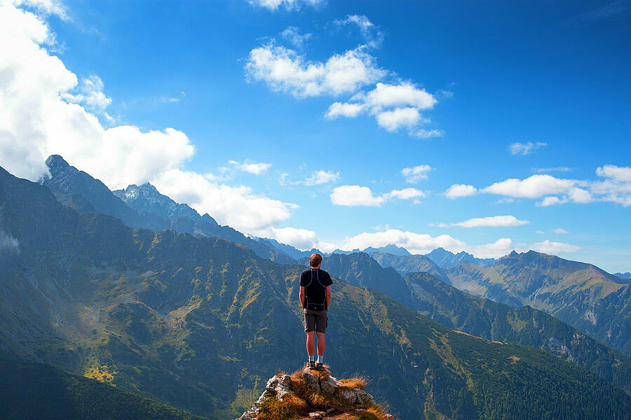 Wandelaar op een bergtop met panoramisch uitzicht op het berglandschap van de Midi-Pyrénées onder een deels bewolkte blauwe lucht.
