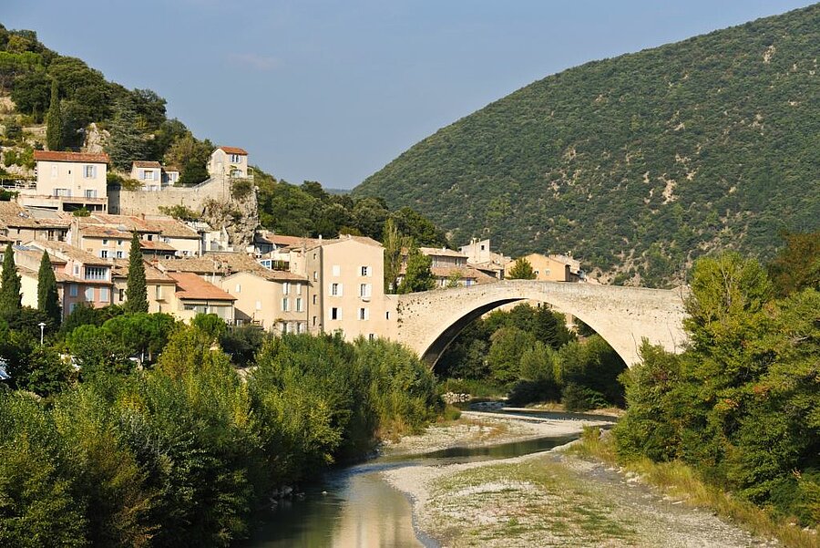 Uitzicht op het dorp Nyons en zijn middeleeuwse brug over de rivier, omringd door de groene heuvels van de Drôme Provençale.