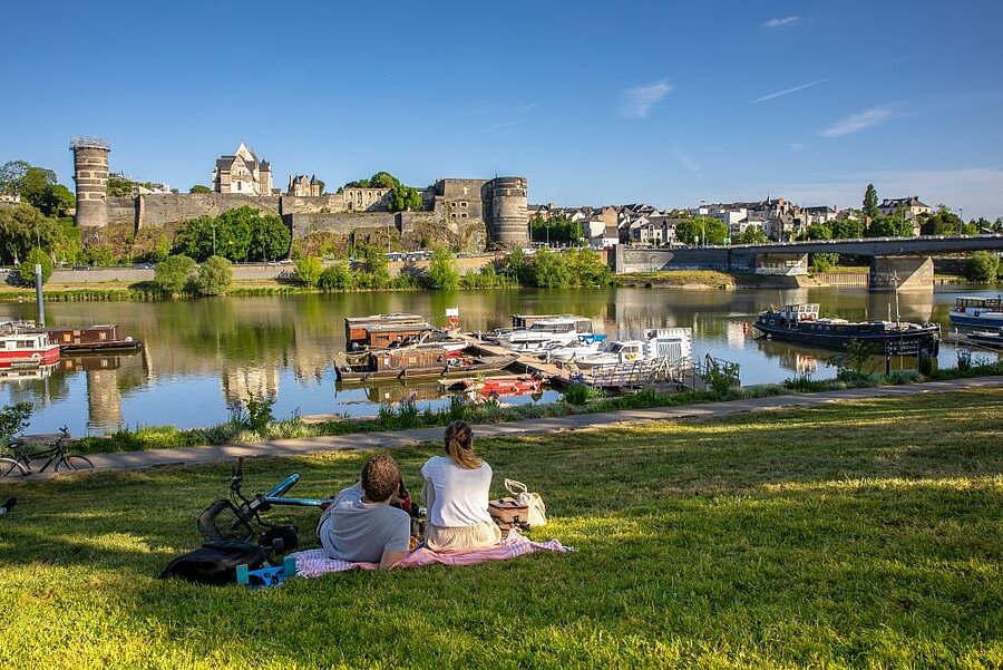 Stelletje op het gras met uitzicht op het kasteel van Angers en boten op de Maine, vlak bij een camping in de Loirestreek.