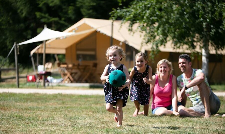 Kinderen spelen voor een lodgetent op de charme camping, lachende ouders, gezinsvakantie in de natuur.