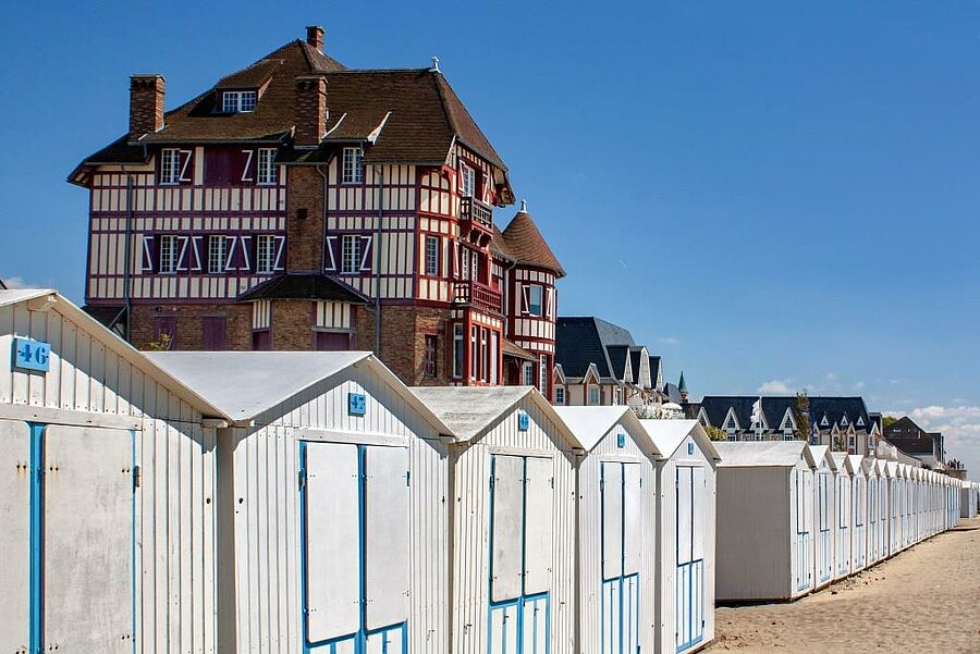 Rij witte strandhuisjes in Le Crotoy met een typische kustvilla op de achtergrond, kenmerkend landschap van de Baai van de Somme.