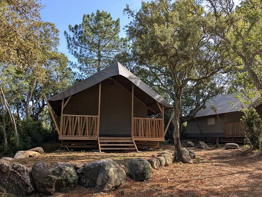 Luxe lodge-tent van hout tussen de bomen in een ecolabel-camping op Corsica, een voorbeeld van duurzaam en milieuvriendelijk verblijven.