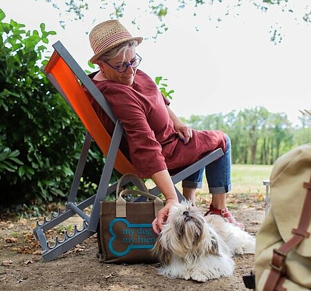 Vrouw ontspant in een ligstoel terwijl ze haar hond aait, op een kleinschalige camping waar huisdieren zijn toegestaan.