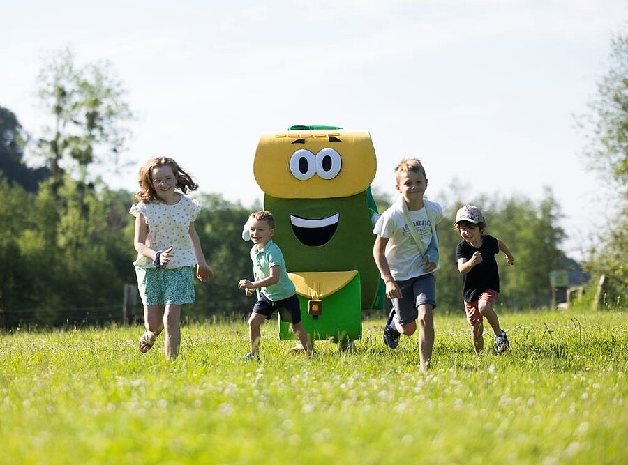 Kinderen rennen in het gras met een mascotte op de camping, gezellige gezinsvakantie midden in de natuur.