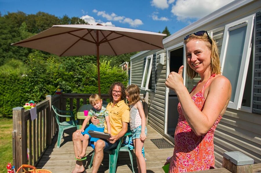 Glimlachend gezin voor een stacaravan, genietend van een voordelige campingvakantie dankzij een budgetvriendelijke formule die past bij een familievakantie.