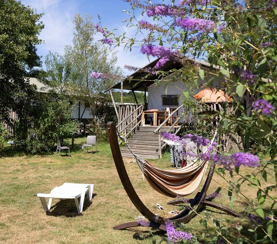Lodgetent van hout met terras, hangmat en ligstoel in een bloementuin op een natuurcamping bij Angers.