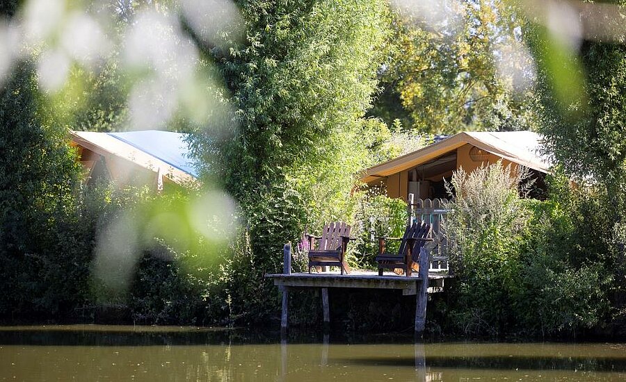 Lodgetent met houten terras en stoelen aan een rustige vijver op een natuurcamping in Pays de la Loire.
